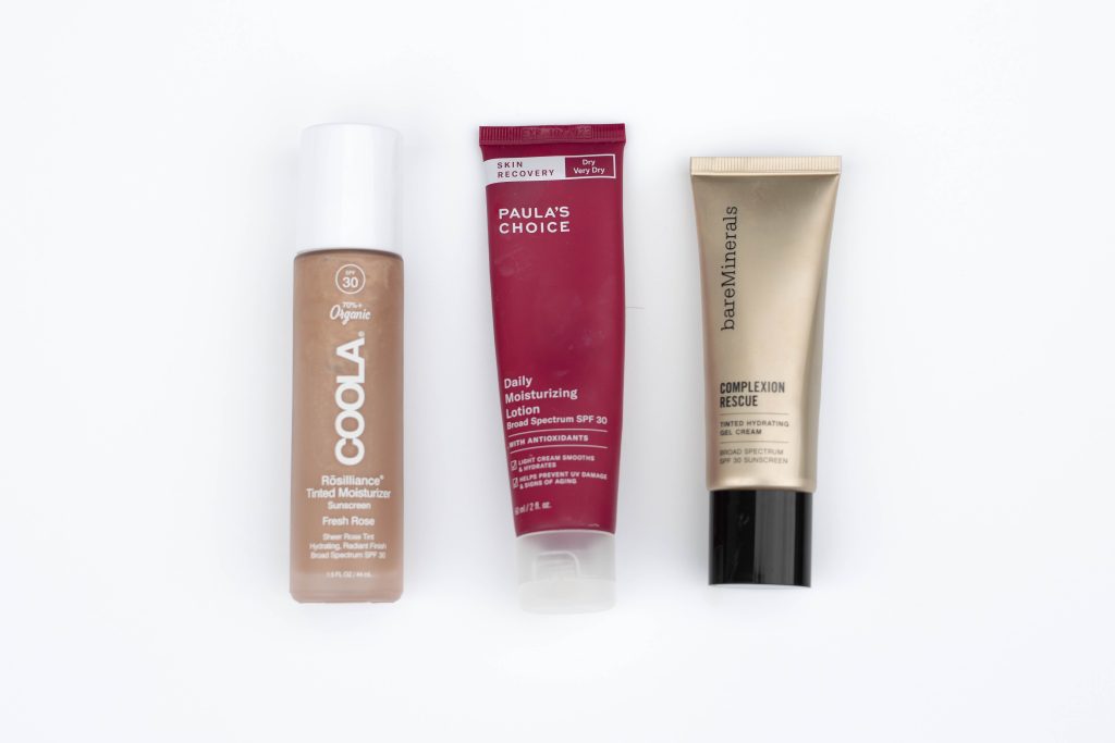 Three bottles of sunscreen lined up on a white background
